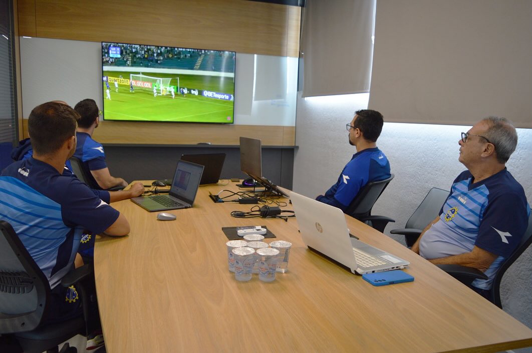 Na imagem há 4 dirigentes do São José EC assistindo um lance de um jogo em uma tv.