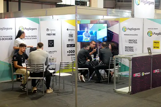 Estande da PagSeguro na área B2B da Brasil Game Show 2025, com grupos de profissionais conversando em mesas sobre soluções de pagamento e parcerias estratégicas.