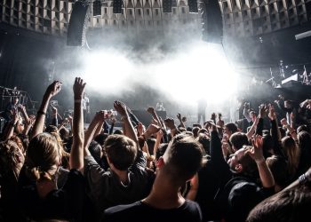 Público lotado dançando em um club com iluminação intensa durante apresentação de música eletrônica.